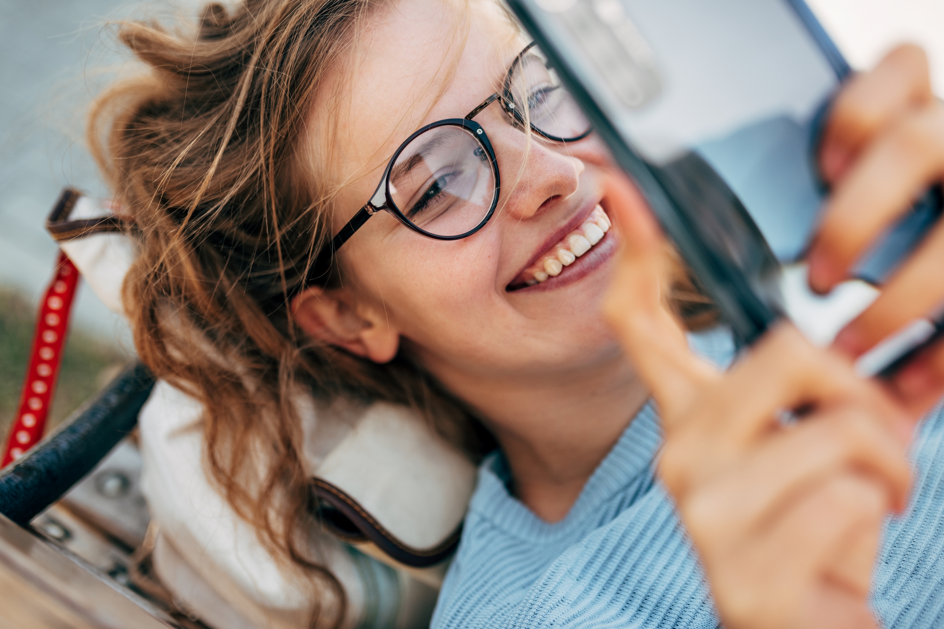  A cheerful woman wearing glasses holds a cell phone, showcasing a warm smile and a friendly expression.